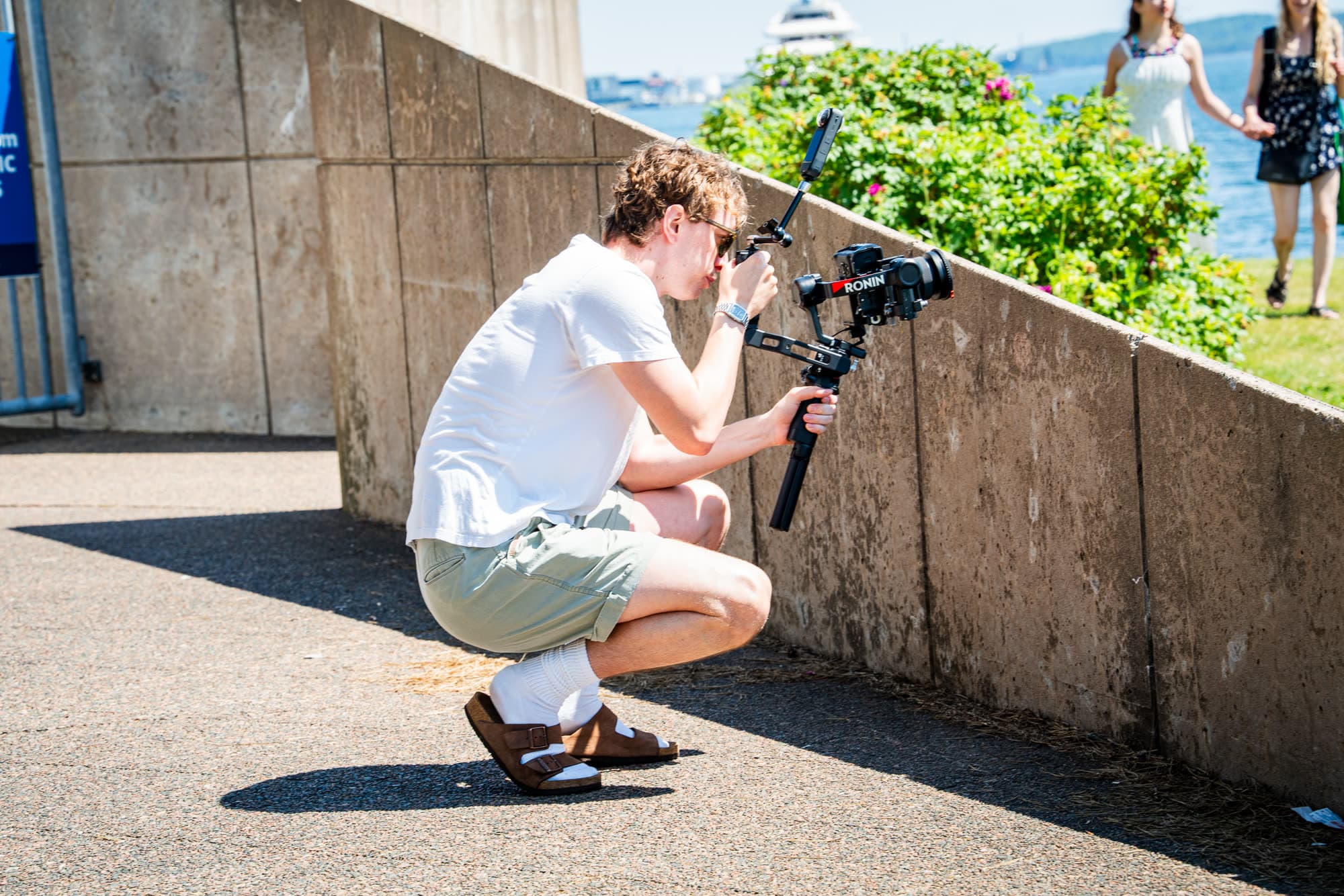 A videographer crouched low for a shot by the water
